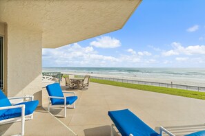 A patio with lounge chairs and a table overlooking a beach. - Oceanfront 2BR Condo Ponce Inlet Sleeps 6 (Ponce Inlet)