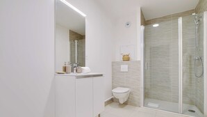 Een moderne badkamer met een douchecabine, een toilet en een wastafel met spiegel.