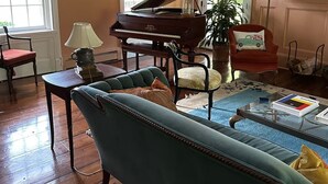 Una sala de estar con un piano de cola, un sofá color turquesa, una mesa de centro con libros y un sillón rojo.
