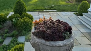 Una jardinera de piedra con suculentas, un granero rojo y un césped bien cuidado.