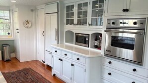 Una cocina con armarios blancos, microondas, horno y una alfombra estampada.