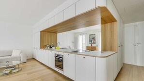 A modern kitchen with white cabinetry, a wooden accent, a built-in oven, and a glass coffee table. - Beautiful Apartment - 1br- 4P - Sacre-coeur (Paris)