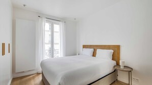 A bedroom with a bed, a bedside table, a window with curtains, and a door. - Beautiful Apartment - 1br- 4P - Sacre-coeur (Paris)