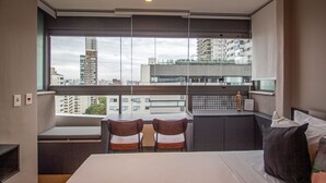 Hotellihuone, jossa on suuri ikkuna, sänky, työpöytä, kaksi tuolia ja näkymä kaupungin ylle.
