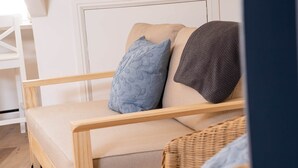 A wooden-framed sofa with a beige cushion, a blue patterned pillow, and a gray knitted throw. - Surf Loft Steps From The Beach (Newquay)