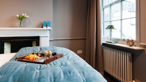 A bedroom with a bed, a bedside table with a lamp, a window with curtains, a radiator, and a fireplace. - The Cleveland Arms II (London)