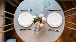 A round table with two white plates, a glass, a knife, a fork, and a vase with pink roses. - The Cleveland Arms II (London)