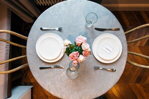 A round table with two white plates, a glass, a knife, a fork, and a vase with pink roses. - The Cleveland Arms II (London)