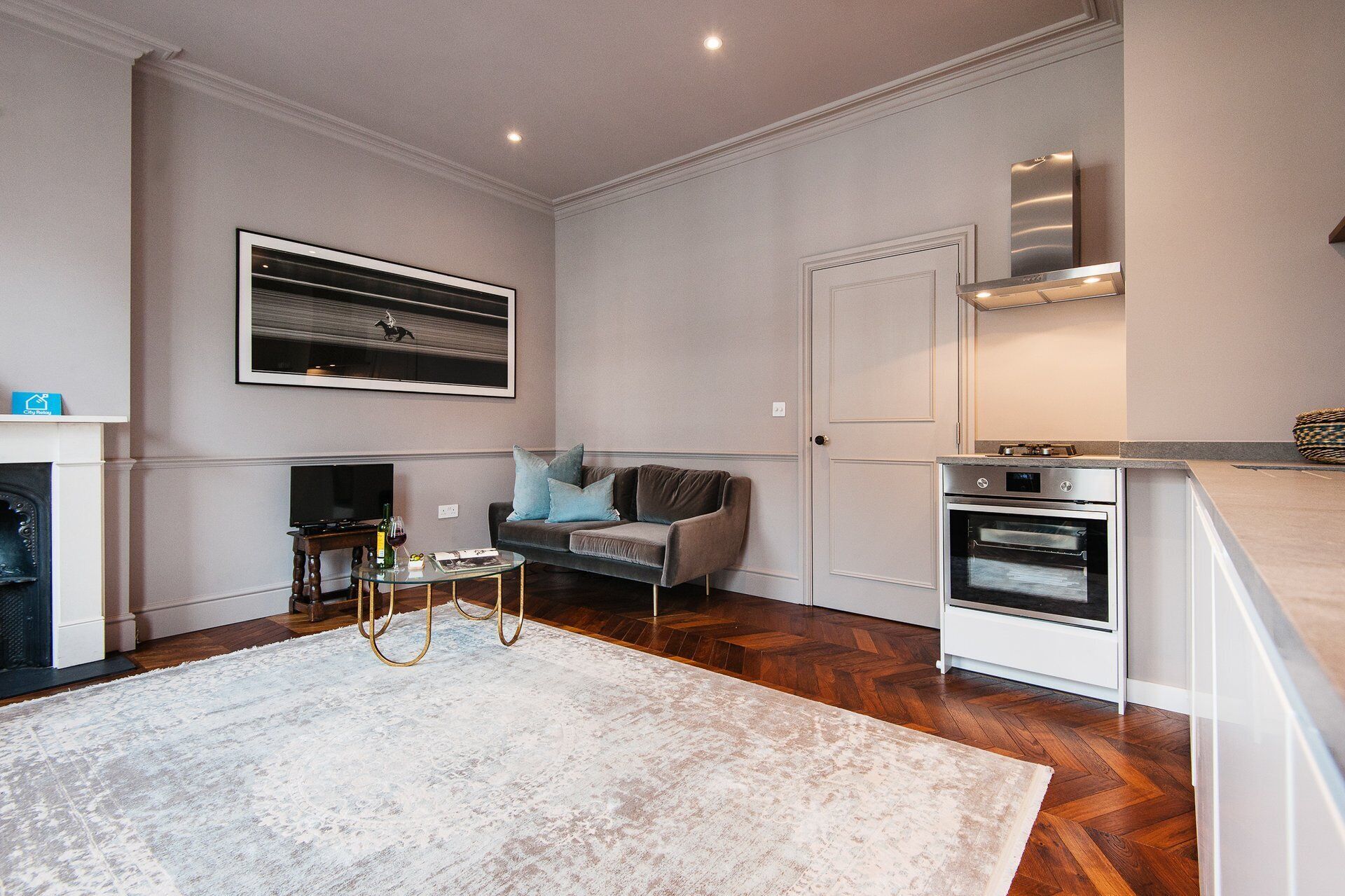 A modern living room with a sofa, a glass coffee table, a fireplace, and a kitchen area with an oven.