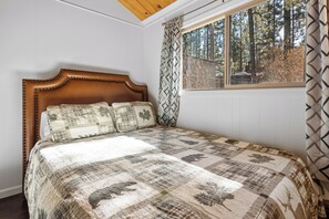 Une chambre à coucher avec une tête de lit en bois, une couvre-lit matelassée et une fenêtre donnant sur les arbres.