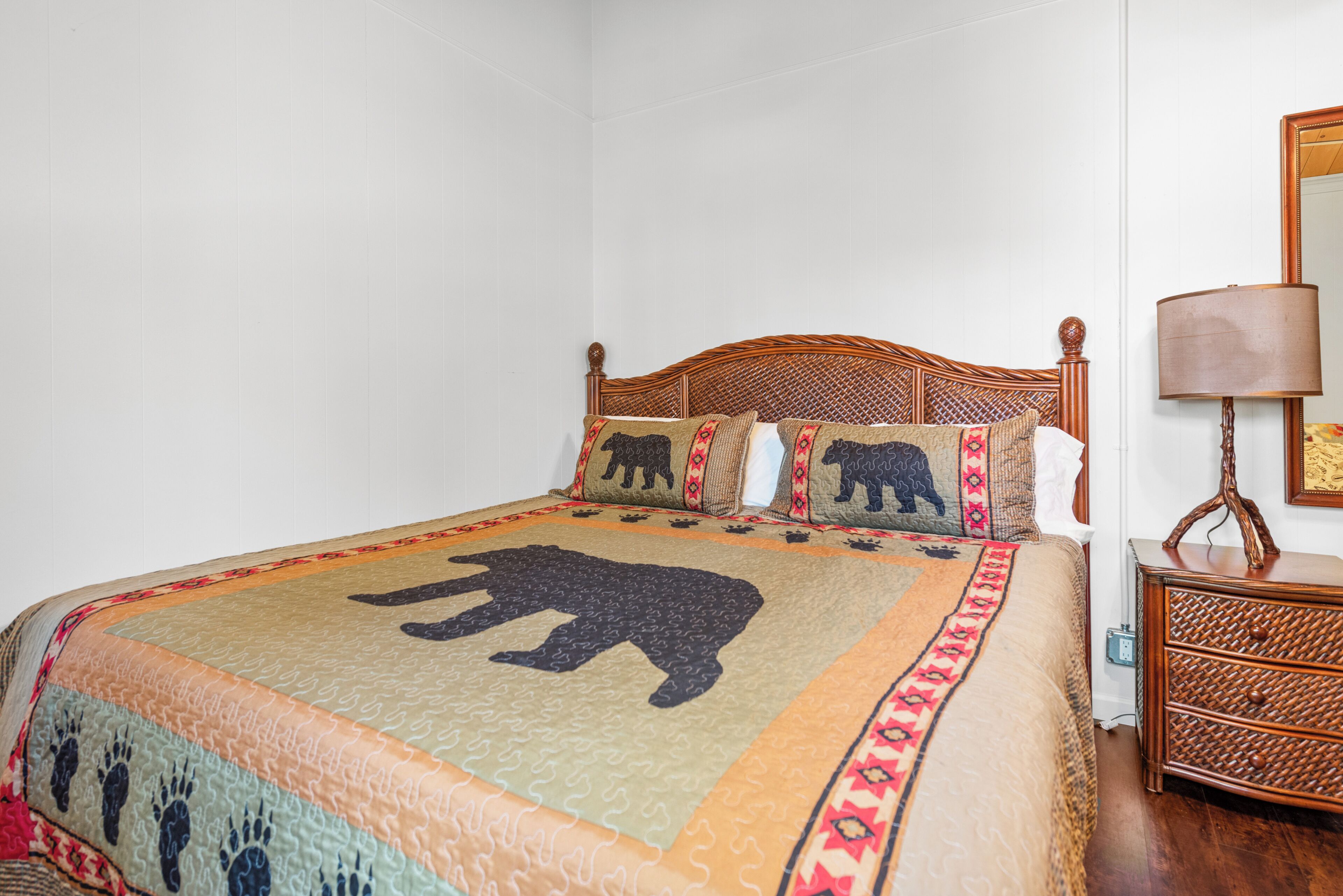 A bed with a quilt featuring a bear design, a wooden headboard, and a bedside table with a lamp.
