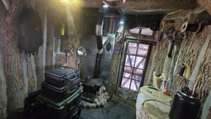 A rustic room with a stone wall, a wooden door, and a window. There are suitcases, a kettle, and a water container on the floor. - Private camground with cabin and spots for 3-4 tents (Beaverton)