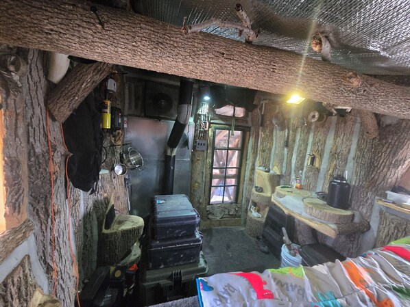 Una habitación rústica con paredes que evocan a árboles, una ventana y una estufa.