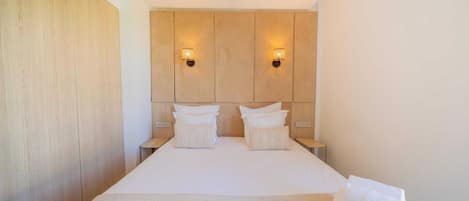 Una habitación de hotel con una cama grande, dos mesitas de noche y dos luces fijadas en la pared.
