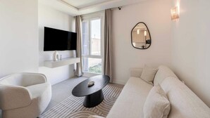A modern hotel room with a flat-screen TV, a sofa, a chair, a round coffee table, a large mirror, and a window with curtains. - Charming Apartment - 2bdr/6p - Saint Tropez/port (Saint-Tropez)