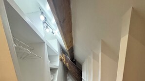 Un corridoio stretto con pavimento in legno, scaffali bianchi e un soffitto spiovente con travi a vista.
