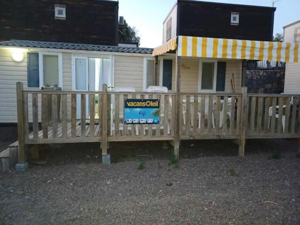 Een houten hek met een bord voor 'Vacansoleil' en een klein gebouwtje met een gestreepte luifel.