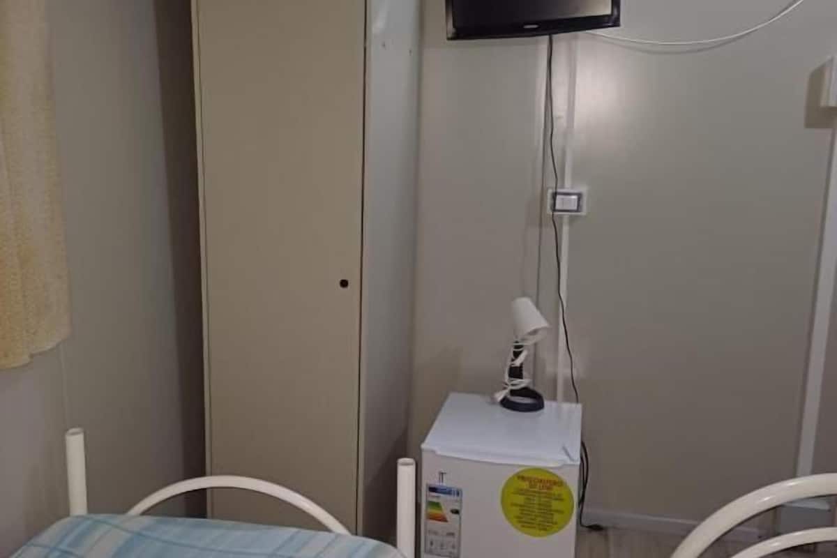 A small room with a bed, a wardrobe, a desk with a lamp, and a TV mounted on the wall.
