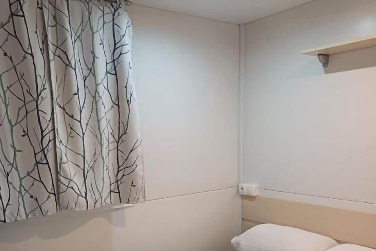 A single bed with white linens, a folded towel, and a wall-mounted shelf.