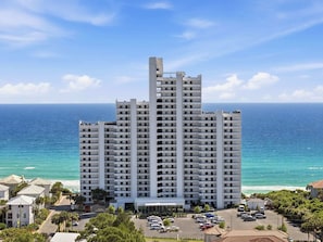 A high-rise hotel with multiple floors, a parking lot, and a view of the ocean. - Diamonds on the Water- Luxury 16th-Floor Gulf Views (Santa Rosa Beach)