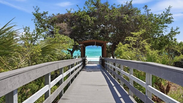 Une promenade en bois menant à une plage, avec une arche en bois à l’entrée.