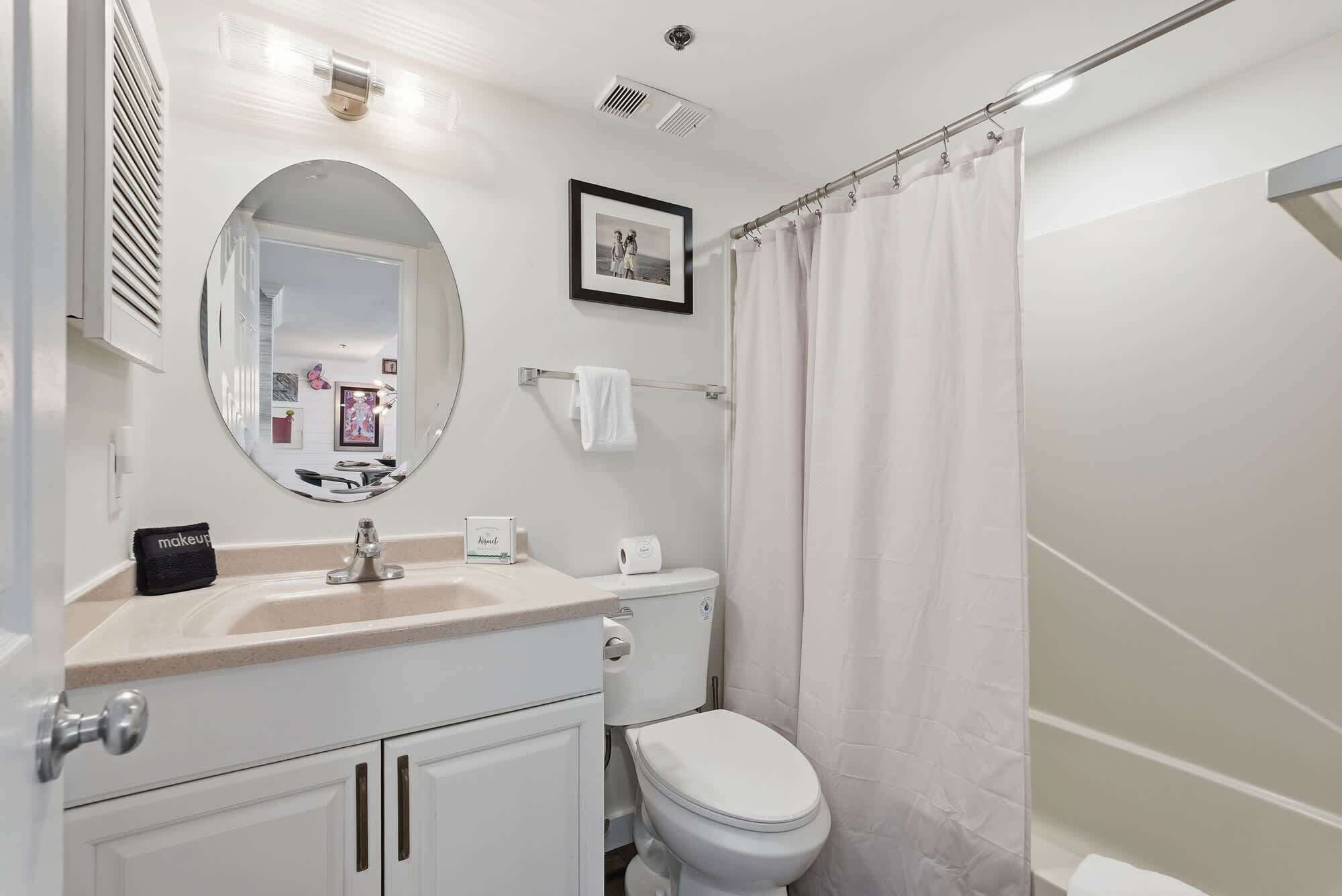 Un baño con lavamanos, espejo, inodoro y cortina de ducha.