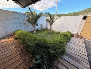 A garden area with a wooden deck, potted plants, and a white wall. - Tenexia – Cozy Studio La Gaulette | 5 min from Le Morne (La Gaulette)