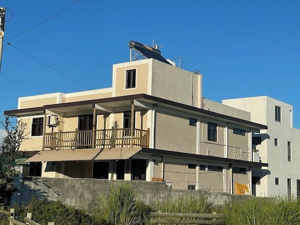 A modern two-story building with a balcony, a satellite dish, and a concrete wall in the foreground.