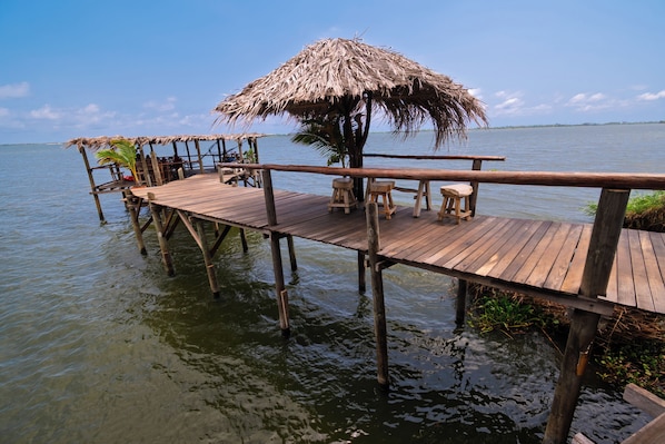 A wooden pier extending into calm water, with thatched umbrellas and seating. - Villas Isla Montosa (Coyuca de Benítez)