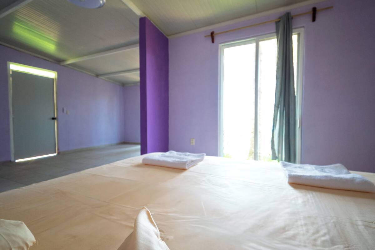 Ein Zimmer mit einem großen Bett, einem Fenster mit Vorhängen und einer Tür.