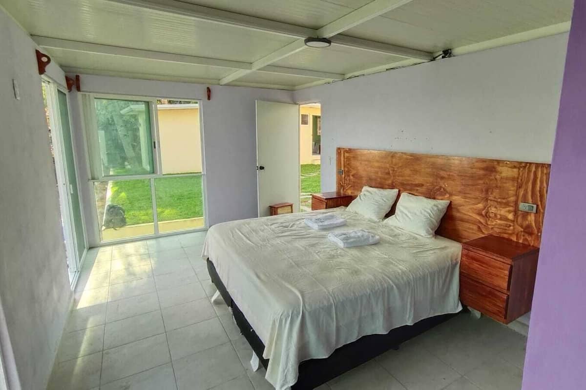 Ein Schlafzimmer mit einem Bett, einem Holzkopfende, Nachttischen und Blick durch eine Glastür.