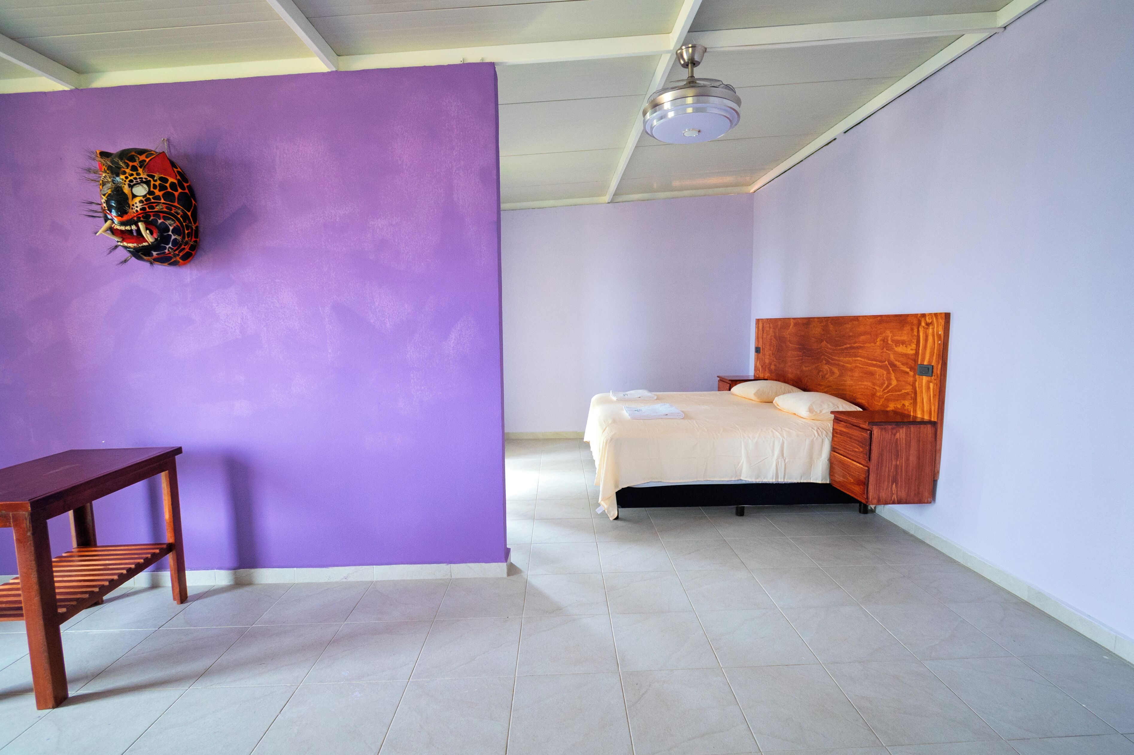 Un dormitorio con cama, una mesita de noche de madera, una pequeña mesa y un ventilador de techo.