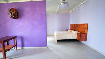 Un dormitorio con cama, una mesita de noche de madera, una pequeña mesa y un ventilador de techo.