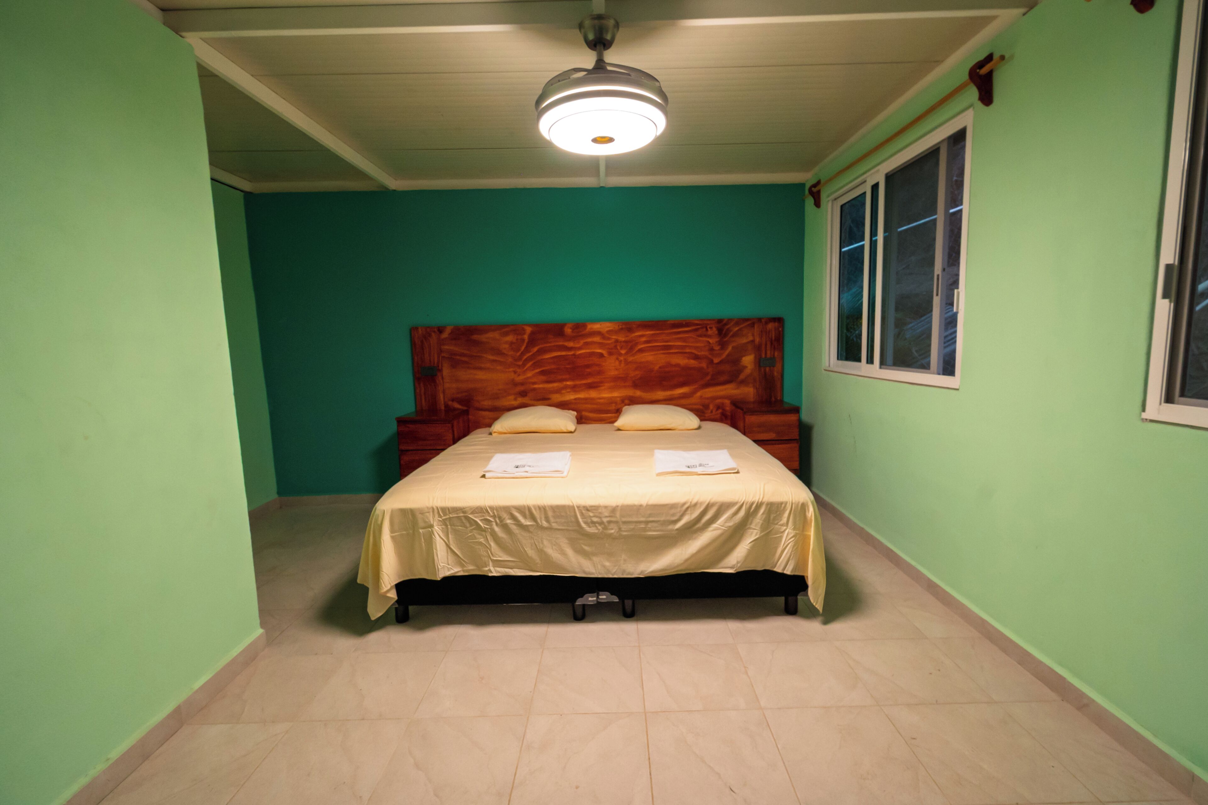 Una habitación con cama, ventilador de techo y ventana.