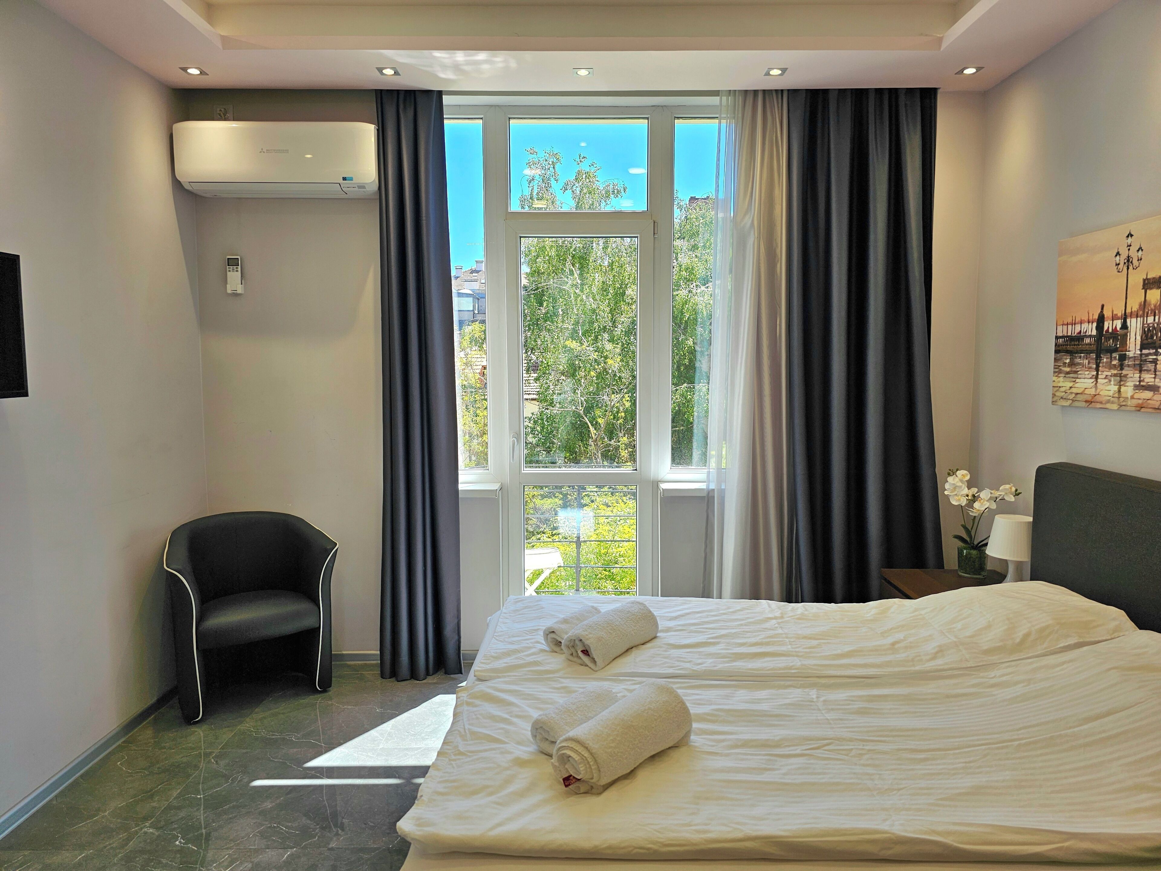 Quarto de hotel com cama, uma cadeira, ar condicionado e janela com cortinas.