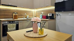 A modern kitchen with wooden cabinets, a built-in oven, a sink, and a flat-screen TV mounted on the wall.