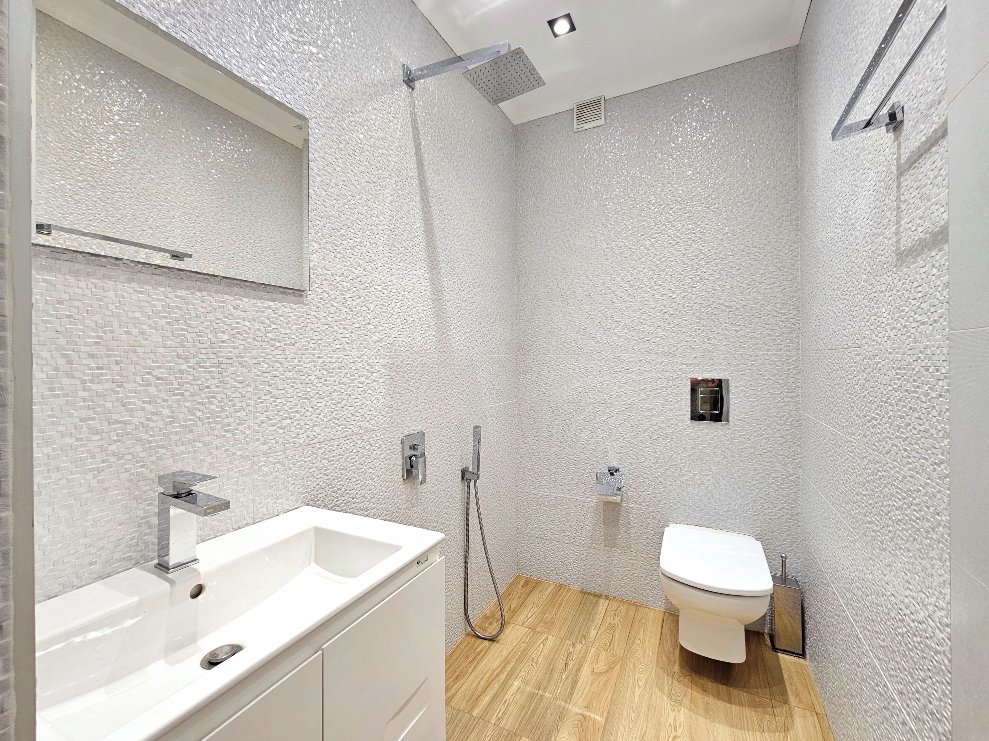 A modern bathroom with a white sink, shower, and toilet.