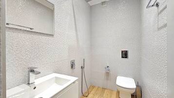 A modern bathroom with a white sink, shower, and toilet.