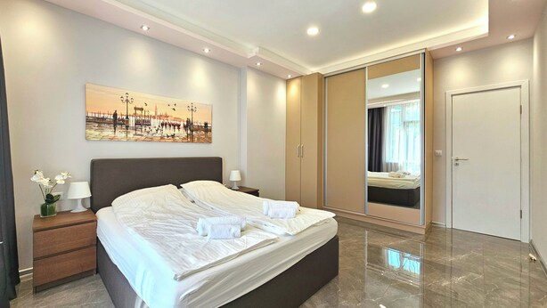 A modern bedroom with a large bed, a nightstand, a mirror, and a painting on the wall.