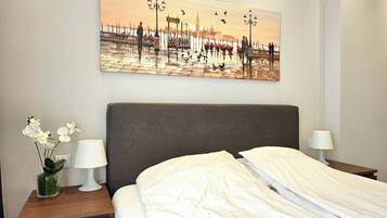 Una camera d'albergo con un letto, comodini, un vaso con fiori e un quadro che raffigura un panorama urbano.