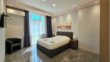 A modern hotel room with a large bed, a bedside table, a chair, and a painting on the wall.
