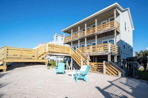 A beachfront property with a wooden deck, two chairs, and a staircase leading to a balcony. - On Porpoise- Oceanfront, Pet Friendly (North Topsail Beach)