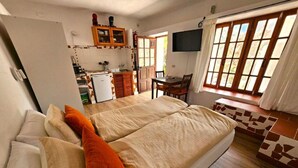 Un dormitorio con cama, almohadas, televisor, kitchenette pequeño y ventana.