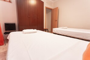 Quarto de hotel com duas camas de solteiro, um guarda-roupa de madeira, uma mesa pequena e uma cadeira.