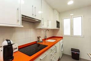Eine Küche mit weißen Schränken, einer orangefarbenen Arbeitsplatte, einer Kaffeemaschine, einer Mikrowelle, einem Spülbecken und einem Mülleimer.