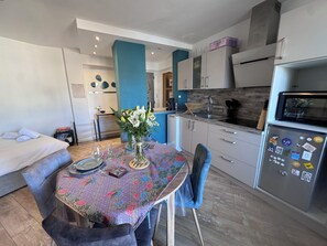A modern kitchen with a dining table set for two, a refrigerator with magnets, and a blue accent wall. - Charming apartment - Centre Cannes - Near Palais des Festivals and beaches (Cannes)
