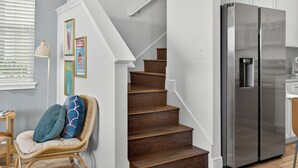 A staircase with wooden steps, a wicker chair with cushions, a stainless steel refrigerator, and white cabinets. - Waterfront 3BR Pool Cottage at Margaritaville Orlando - Near Disney (Kissimmee)