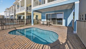 A pool area with a brick deck, a pool, and a building with balconies and a covered patio. - Waterfront 3BR Pool Cottage at Margaritaville Orlando - Near Disney (Kissimmee)