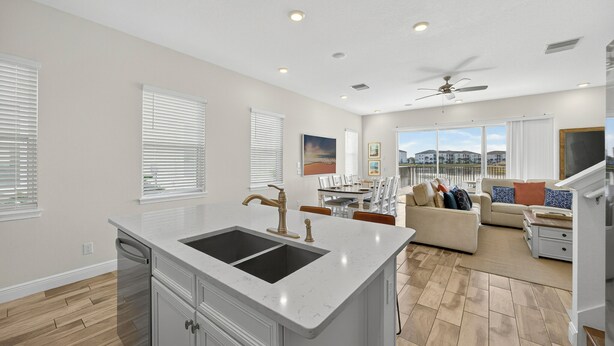 A modern kitchen with a large island, a dining area with a table and chairs, a living room with a sofa and a TV, and a ceiling fan. - Waterfront 3BR Pool Cottage at Margaritaville Orlando - Near Disney (Kissimmee)