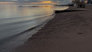 Ranta, jossa on puinen laituri, tyyni meri ja auringonlasku.